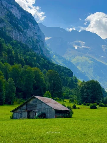 Wooden barn in a meadow beneath towering cliffs