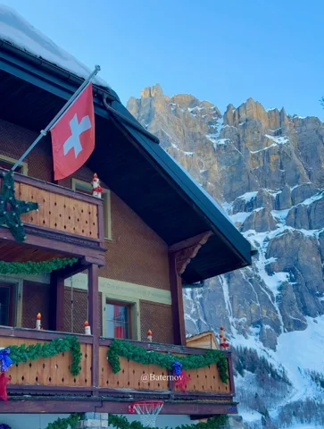 Swiss flag on a chalet beneath a snowy rock face