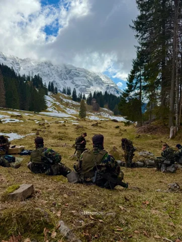 Soldiers resting on a grassy slope beside conifers