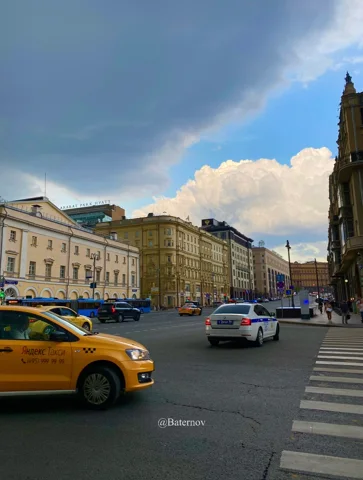 Cars and a yellow taxi on a city street beneath clouds