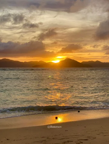 Sunset behind distant mountains across a sandy bay