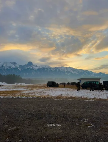 Vehicles on open ground beneath an evening mountain sky