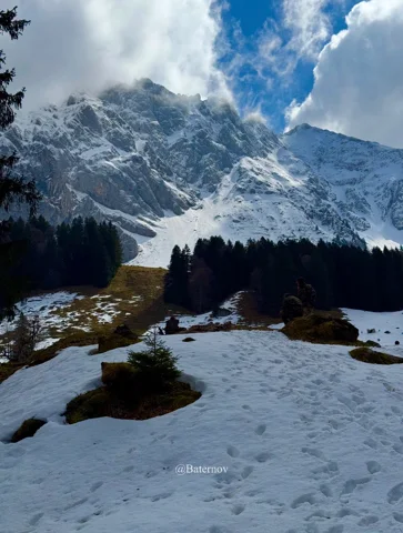 Snowy clearing below a steep cloud-covered mountain