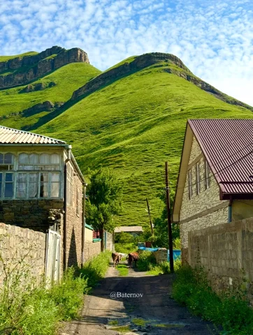 Narrow village lane beneath a steep green hill