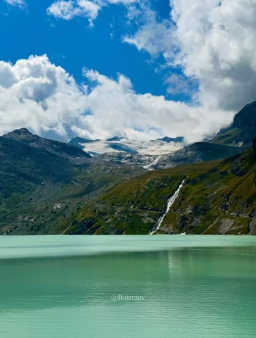 Pale mountain lake beside a waterfall and cloud-covered peaks