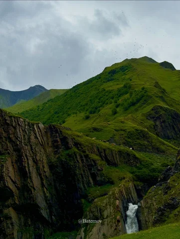 Waterfall beneath dark cliffs and green ridges