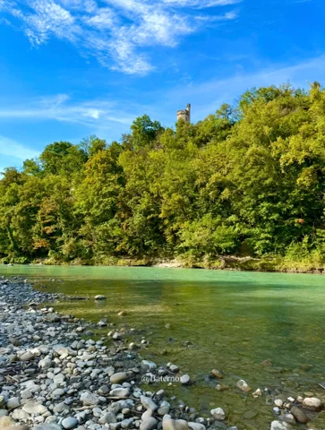Rocky riverbank beside green water and dense trees