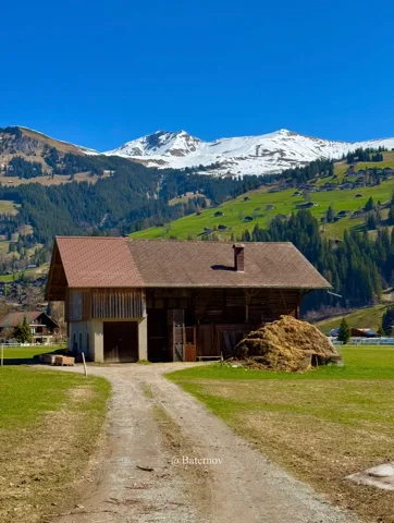 Chalet beside a gravel track beneath snowy mountains