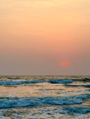 Red sun above waves beneath a hazy sky