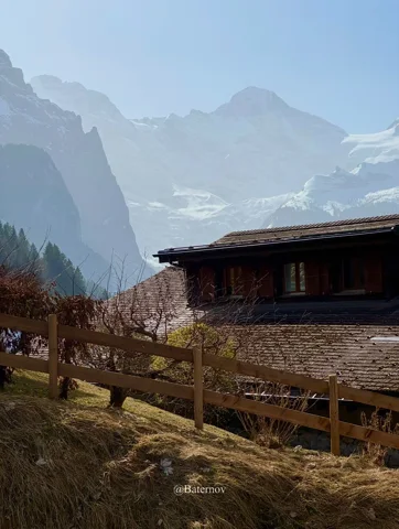 Wooden mountain building and fence beneath hazy peaks