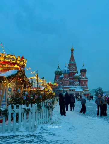 People walking through a snowy square beside festive lights