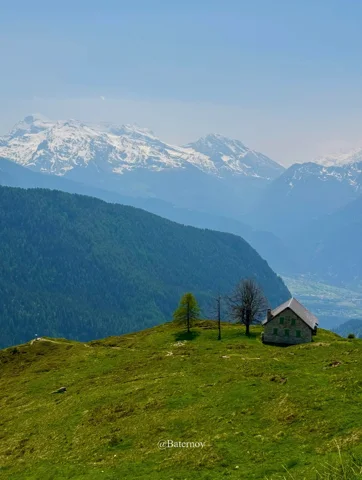 Small chalet on a grassy ridge facing distant snowy mountains
