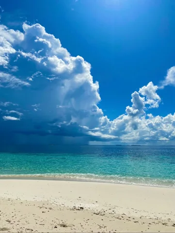 Towering clouds above a pale beach and turquoise sea