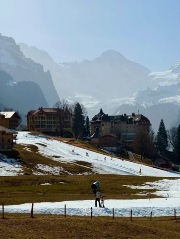 Person crossing a snowy village meadow beneath hazy peaks