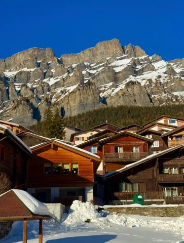 Snow around chalets beneath rocky mountain peaks