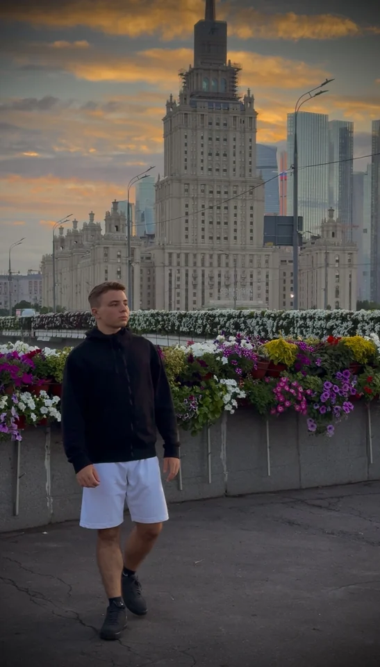 Brandon Alexander Otter standing beside flowers with a tall building behind him.
