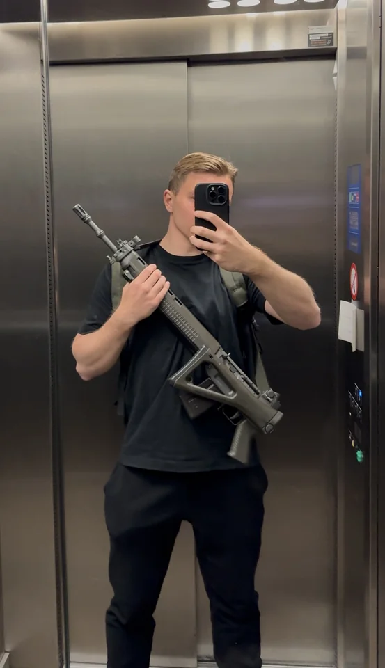 Brandon taking a mirror photograph in a lift while holding a rifle.